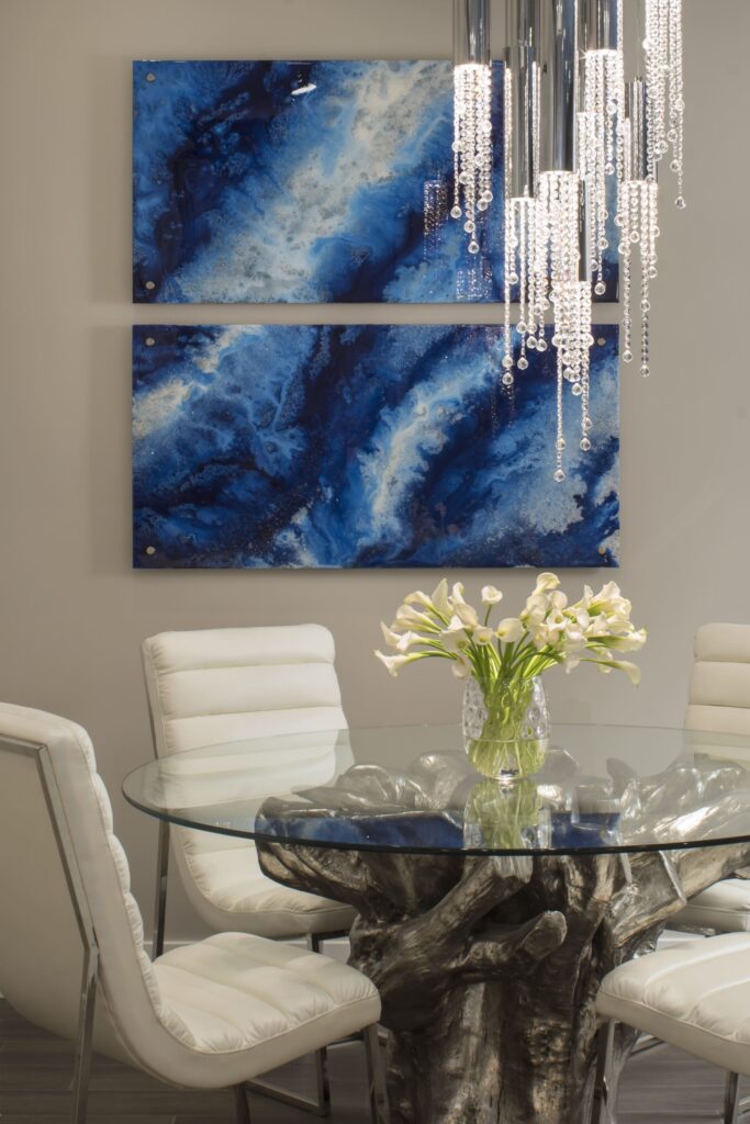 A modern dining area design that features a glass-top table with a sculptural metallic base, surrounded by white cushioned chairs.